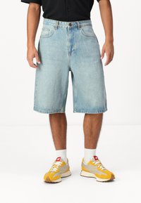 Väldigt blå denimshorts med lös passform, knälång, med framfickor och knappgylf. Tillsammans med gula och grå sneakers.