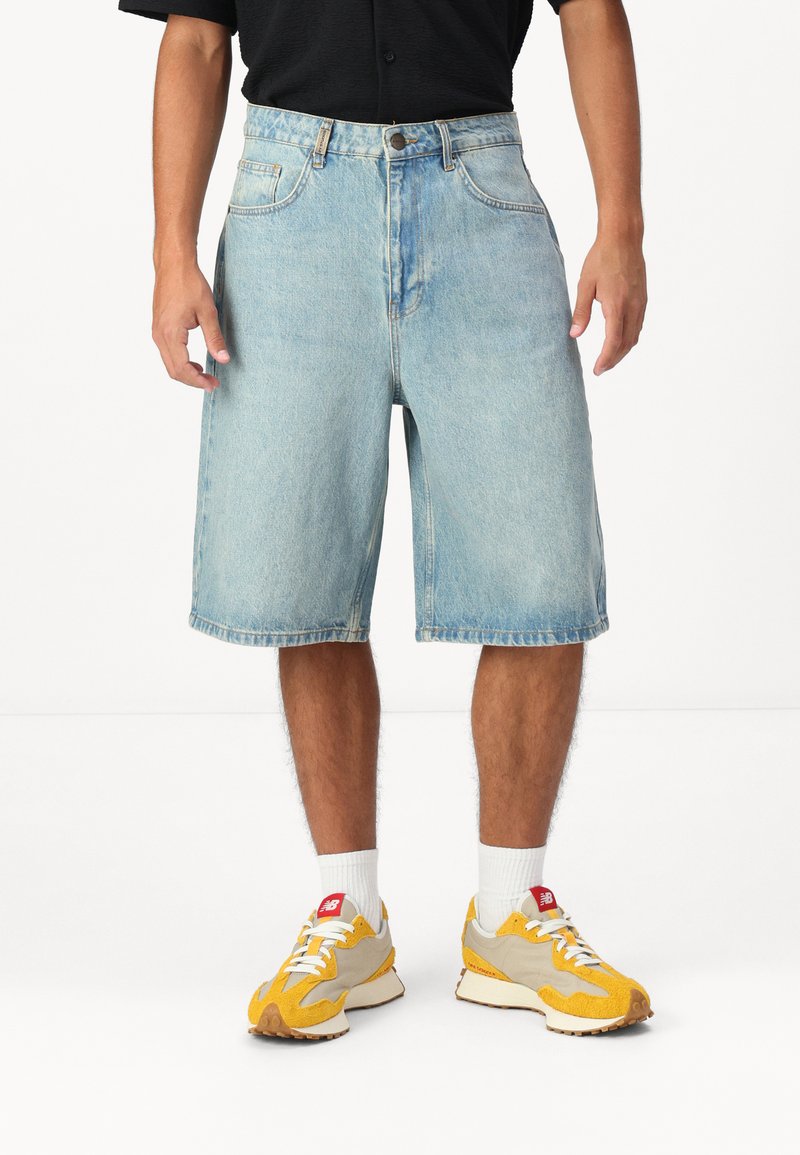 Väldigt blå denimshorts med lös passform, knälång, med framfickor och knappgylf. Tillsammans med gula och grå sneakers.