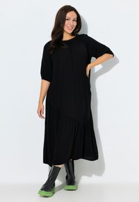 Vestido midi negro de corte holgado, con mangas cortas abullonadas, escote fruncido y dobladillo en capas. Combinado con botas negras de suela verde.