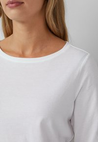 Witte, lange mouwen top met een gladde textuur en een ronde hals. Eenvoudig ontwerp met minimale details en een comfortabele pasvorm.