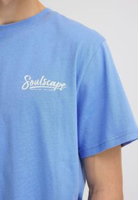 T-shirt en coton bleu à manches courtes, avec un logo imprimé blanc "Soulscape" sur le côté gauche de la poitrine. Texture lisse, coupe décontractée.