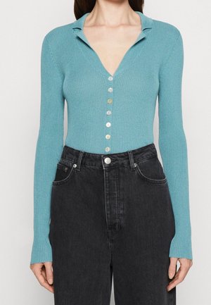 Turkos randig cardigan med djup V-ringning, långa ärmar och sju knappar i varierande färger, kombinerad med högmidjade svarta jeans.