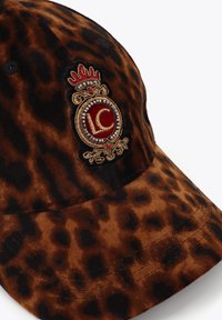 Cappellino con stampa leopardata marrone realizzato in tessuto morbido, con un emblema ricamato rosso e oro con design di corona sulla parte anteriore.