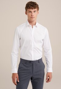 Witte lange mouwen shirt met een puntige kraag en knoopsluiting, gecombineerd met donkergrijze broek met een voorzak en een plat voorkant ontwerp.