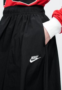 Crne Nike kratke hlače s elastičnim pojasom, s bijelim Nike logotipom s lijeve strane, glatke teksture i bočnim džepovima.