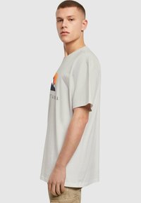 Camiseta de manga corta en gris claro con un diseño gráfico colorido de montañas y texto. Fabricada en algodón, tiene un ajuste relajado y una textura suave.