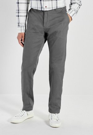 Pantaloni di cotone grigi con una finitura testurizzata, dotati di tasche laterali e design a gamba dritta, abbinati a sneakers bianche.