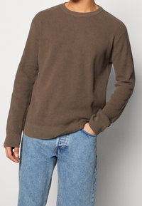Brun ribbad stickad tröja med rund halsringning och långa ärmar, kombinerad med ljusblå denimjeans. Tyget har en strukturerad yta.
