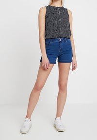 Blå denimshorts med en åtsittande design, i kombination med en ärmlös svart topp med ett litet vitt prickigt mönster och gatherad halsringning.
