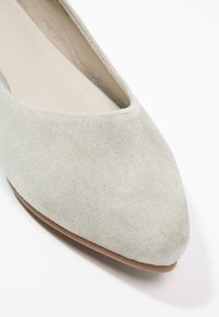 Chaussure plate en daim gris clair à bout pointu avec un empiècement bas et une semelle intérieure beige lisse sur fond blanc.