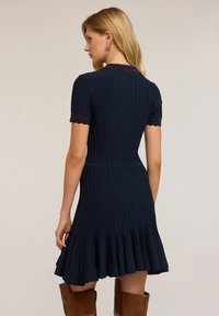Robe rayée bleu marine à manches courtes, avec des poignets scallopés et un ourlet évasé. La bordure rouge contrastante sur le col et les manches ajoute du détail.