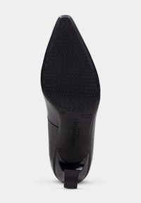 Svart högklackad skosula med spetsig form, texturerad gummi för grepp och präglad logotyp. Ren design med minimala accenter.