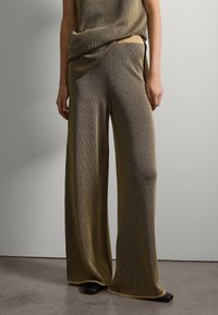 Pantalones de punto de pierna ancha en tonos bronce y dorado con textura de canalé. Presentan una cintura alta y un detalle en negro en el dobladillo.