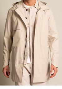 Beige vattentät trenchcoat med huva, har en framsida med dragkedja, bröstficka och en avslappnad passform. Strukturerad tyg med slät yta.