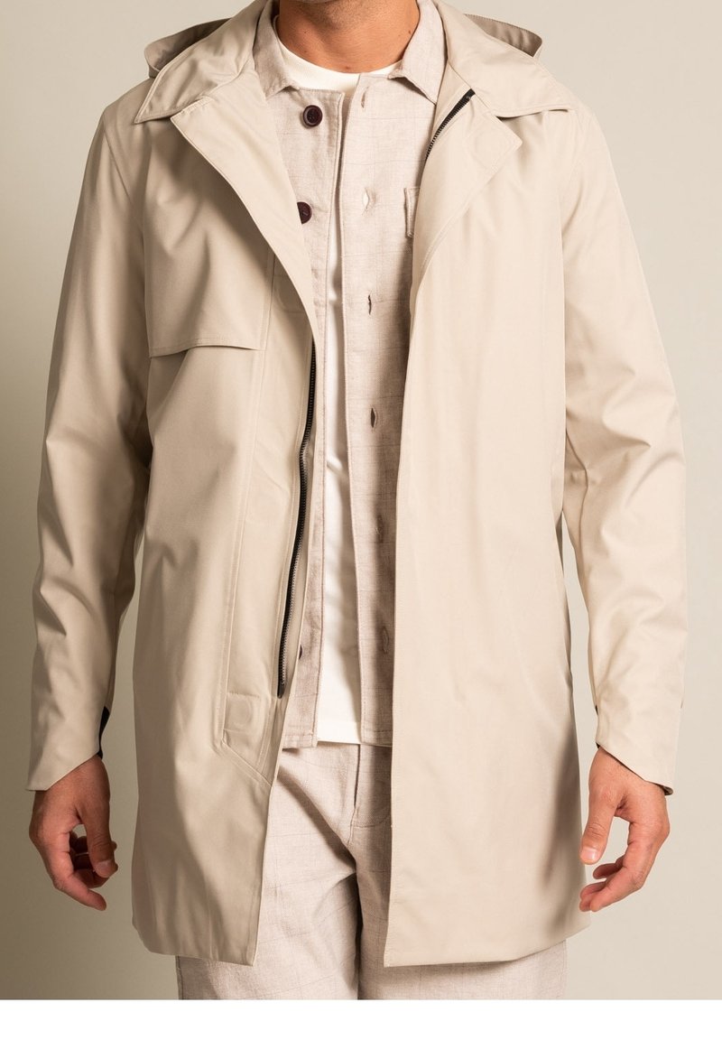 Beige vattentät trenchcoat med huva, har en framsida med dragkedja, bröstficka och en avslappnad passform. Strukturerad tyg med slät yta.