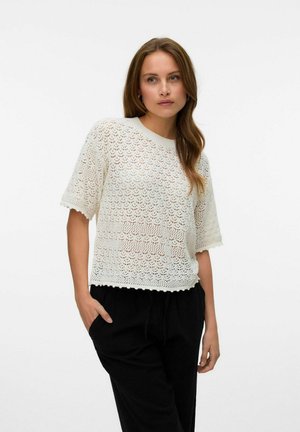 Top en tricot à manches courtes en blanc cassé, présentant des motifs ajourés et des bords festonnés. Associé à un pantalon noir pour un look décontracté.