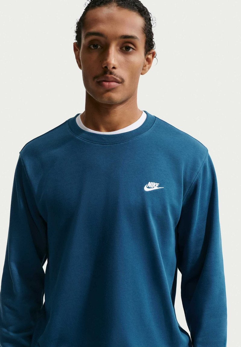 Felpa a maniche lunghe color turchese in tessuto morbido con scollo rotondo e logo Nike bianco sul petto a sinistra. Design semplice, vestibilità comoda.