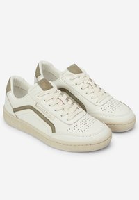 Bílé kožené tenisky s béžovými akcenty, perforovanými detaily, plochými tkaničkami a texturovanou gumovou podrážkou se znakem na boku.