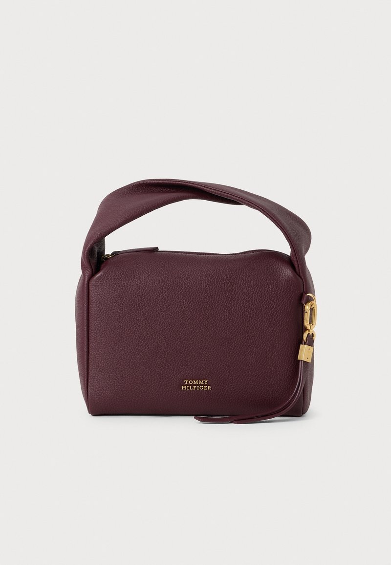 Sac à main en cuir violet foncé avec poignée courte, fermeture éclair dorée et petit détail de verrou doré, avec le logo Tommy Hilfiger sur le devant.