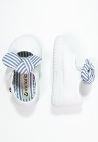 Zapatillas blancas de lienzo con un lazo a rayas azul y blanco, que cuentan con un forro interior a rayas y una suela de goma texturizada.