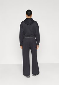 Μαύρο φούτερ με κουκούλα και κορδόνι, συνδυασμένο με παντελόνι φαρδύ σε ίσια γραμμή· και τα δύο κατασκευασμένα από μαλακό ύφασμα με άνετη εφαρμογή και ελαστική μέση.