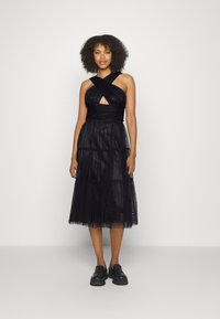 Vestido preto em camadas com corpete cruzado e detalhe em buraco-chave. Feito de tecido leve, apresenta uma cintura ajustada e saia fluida.