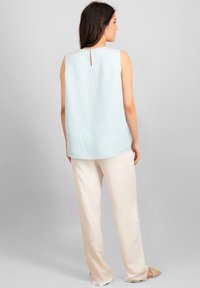 Haut sans manches bleu clair avec un encolure ronde et un petit détail en trou de serrure dans le dos, associé à un pantalon ample de couleur crème.
