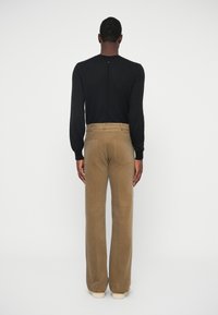 Melnā ribota adīta džemperis ar aizmugures šuvi, saskaņots ar brūnganām dūnu biksēm ar aizmugures kabatām un platām kājām. Beigās apavi noslēdz izskatu.