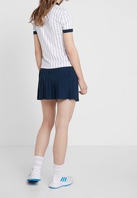 Vit randig pikétröja med marinblå detaljer, kombinerad med en plisserad marinblå kjol. Skorna har vit bas med blå detaljer.