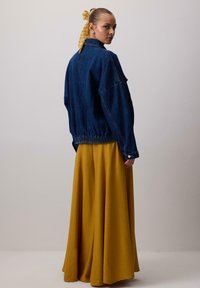 Modrá džínová oversized bunda s elastickým lemem, vrstvená přes dlouhou žlutou sukni. Minimální hardware, jednoduchý design, hladká textura.