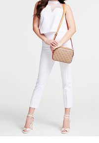 Hvid crop top med gennemsigtig panel, parret med tætsiddende hvide bukser. Brun crossbody taske med logo mønster og hvide strop sandaler.