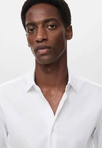 Camicia bianca con colletto strutturato, caratterizzata da una texture liscia e un fit classico. Il tessuto appare leggero e traspirante.