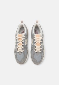 Grå sneakers med overdel i mesh og ruskind, beige detaljer, kremfargede snører og hvit mellomsåle. Har polstret krage og teksturerte detaljer.