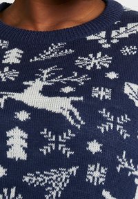 Granatowy sweter typu sweterkowego z białym wzorem renifera i płatków śniegu. Tekstura wydaje się miękka, z prążkowanym dekoltem.