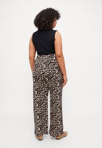 Crna majica bez rukava u kombinaciji s širokim hlačama s leopard uzorkom u smeđoj i crnoj boji. Glatka tekstura; elastična sredina; ravne cipele.