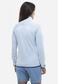 Helles blaues Langarmjackett aus strukturiertem Stoff, mit hohem Kragen und elegantem Design. Kombiniert mit passenden blauen Shorts, zeigt die Rückansicht.