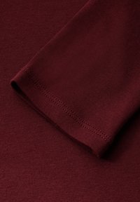 Detail košile s dlouhým rukávem Maroona, vyrobená z hladké a měkké tkaniny s přiléhavým střihem. Spodní okraj a konce rukávů mají úhledné švy.