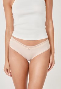 Mutandine nude da donna con texture a coste, bordino in pizzo in vita e un piccolo fiocco decorativo sulla parte frontale. Finitura in tessuto liscia.