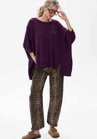 Fioletowy, oversize'owy sweter dzianinowy z okrągłym dekoltem, połączony z szerokimi spodniami w leopardzi wzór. Brązowe buty wsuwane dopełniają stylizację.