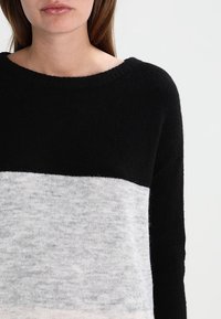 Sweter w czarno-szarą blokową kolorystykę, wykonany z miękkiego materiału, z okrągłym dekoltem i długimi rękawami. Gładka tekstura z kontrastującymi sekcjami.