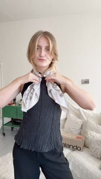 Svart texturerad topp med volang i nederkant, ihop med en ljusfärgad silkscarf med blommönster som knyts runt halsen.