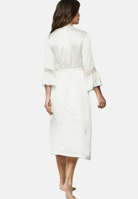 Peignoir en satin blanc avec des manches évasées et des accents en dentelle, noué à la taille, de longueur mi-mollet et de texture lisse.