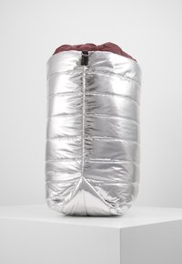 Srebrny insulated plecak o puchatej pikowanej strukturze, okrągłym kształcie, burgundowym wnętrzu i czarnej pętli u góry. Gładka, błyszcząca tekstura.