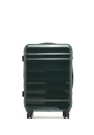 Hard-shell suitcase in dark green, featuring a glossy finish, vertical ridges, and four wheels for mobility. Side handles for easy lifting.