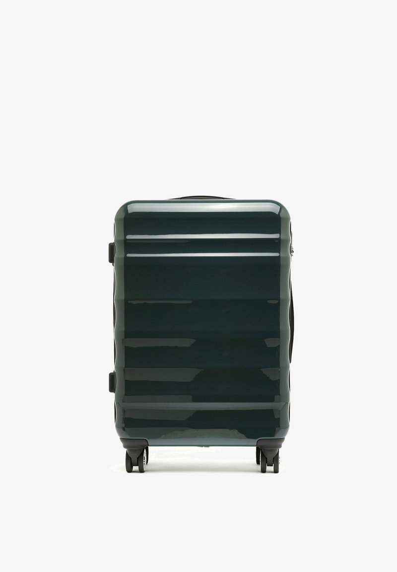 Valigia rigida di colore verde scuro, con una finitura lucida, righe verticali e quattro ruote per la mobilità. Maniglie laterali per un facile sollevamento.