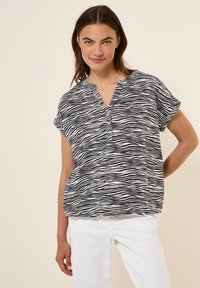Blouse zébrée noir et blanc avec un décolleté en V et des manches courtes, comportant des boutons sur le devant et une coupe ample.