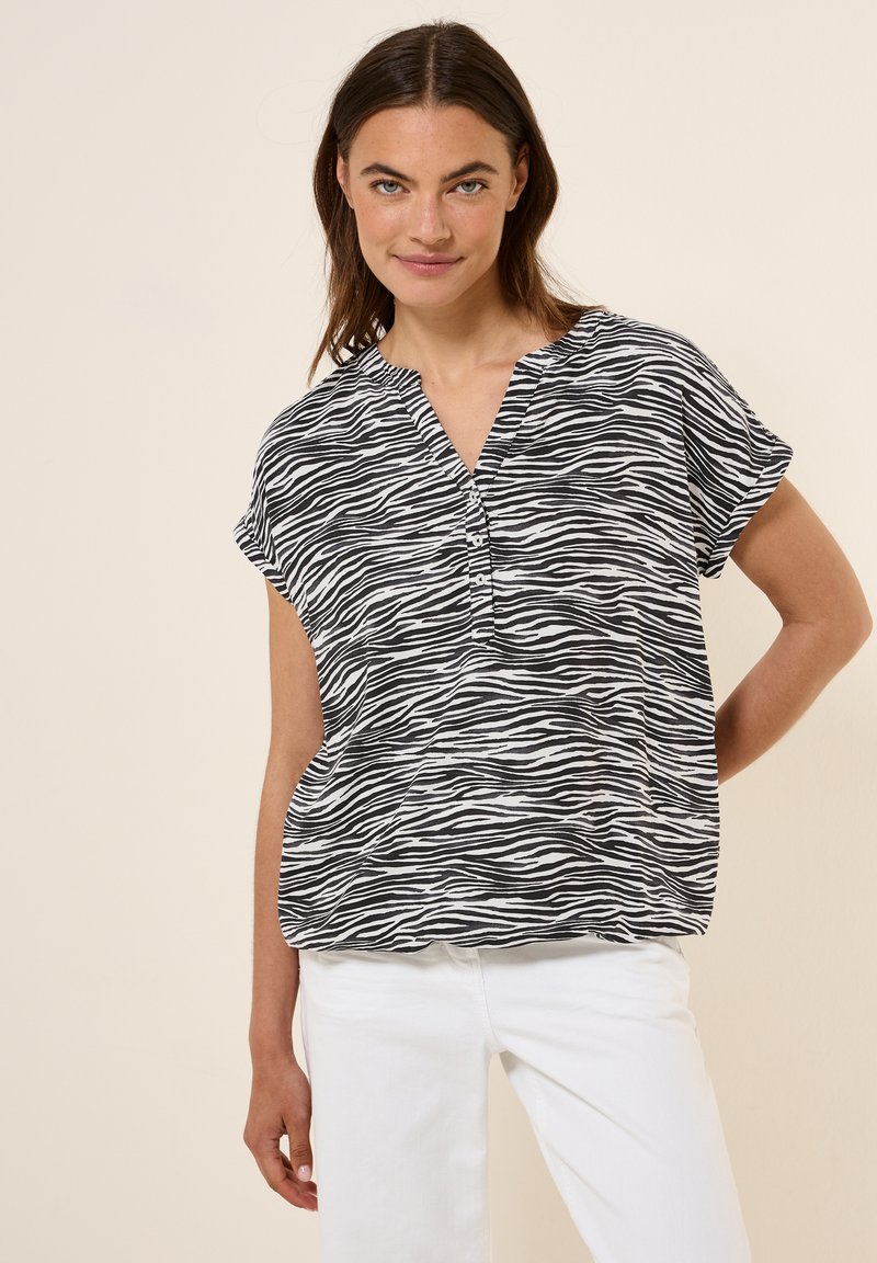 Blouse zébrée noir et blanc avec un décolleté en V et des manches courtes, comportant des boutons sur le devant et une coupe ample.