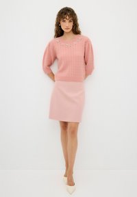 Pull en tricot rose avec des manches courtes bouffantes, agrémenté de décorations florales, associé à une jupe rose ajustée et des chaussures à bout pointu beiges.