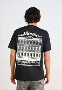 Camiseta negra de algodón con un gran gráfico blanco de un edificio con ventanas arqueadas y el texto "ellesse COURTSIDE CLUBHOUSE" debajo.