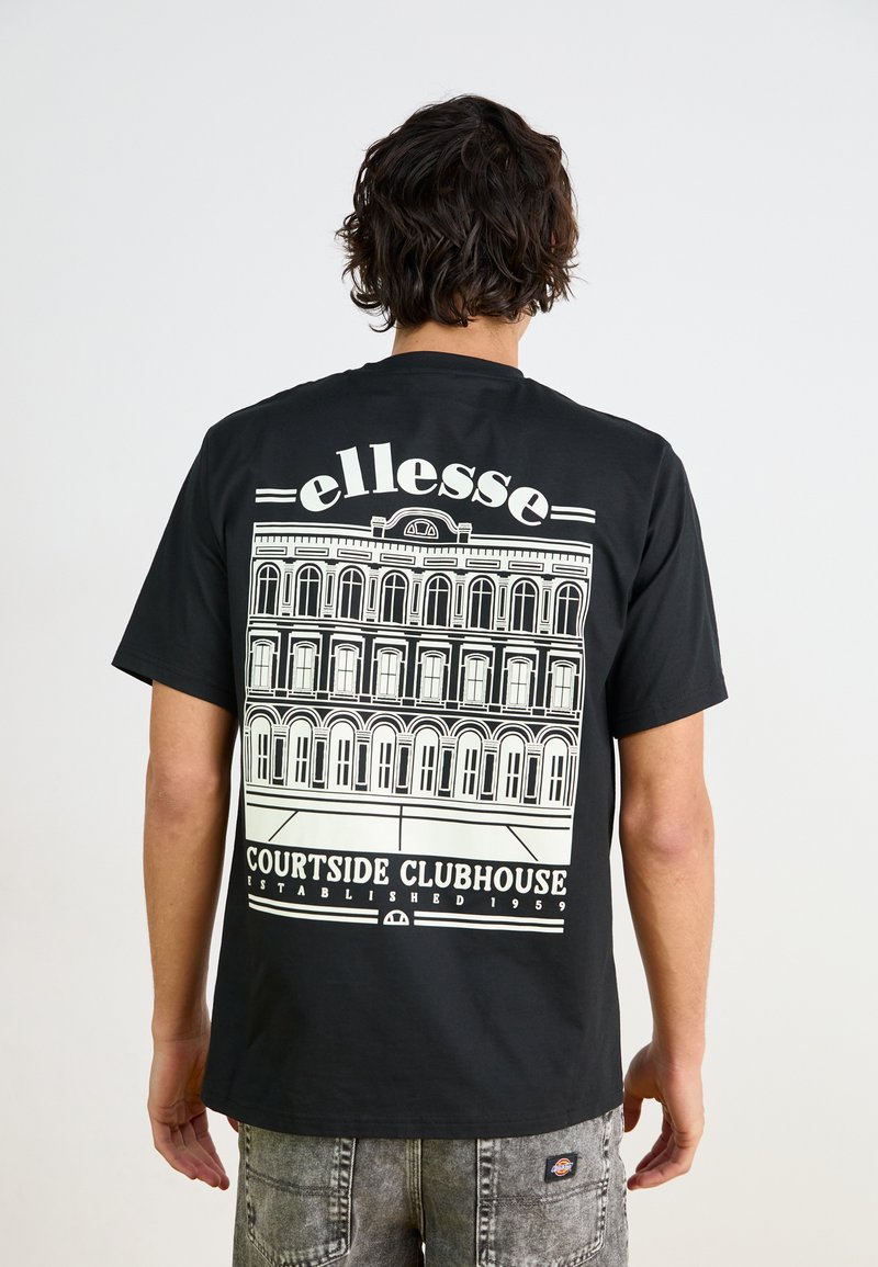 Camiseta negra de algodón con un gran gráfico blanco de un edificio con ventanas arqueadas y el texto "ellesse COURTSIDE CLUBHOUSE" debajo.